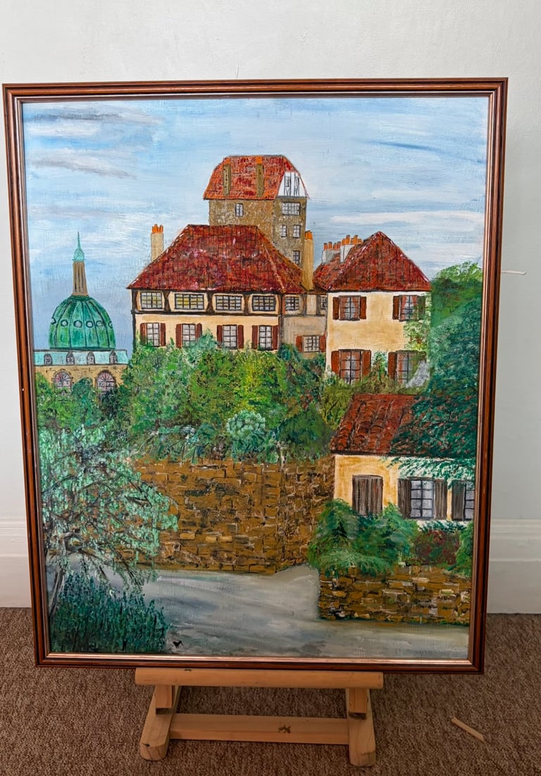 Framed painting of European stone houses on a hillside with a church dome visible in the background, displayed on a wooden easel