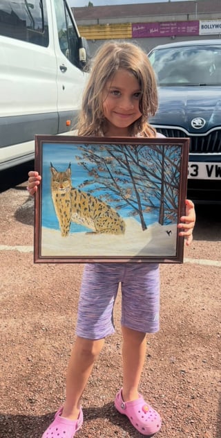 Child holding framed artwork of a spotted lynx in snowy landscape outdoors in parking lot