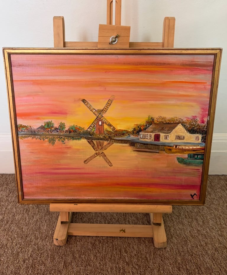 Oil painting on wooden easel depicting a sunset landscape with a windmill and riverside house reflected in water
