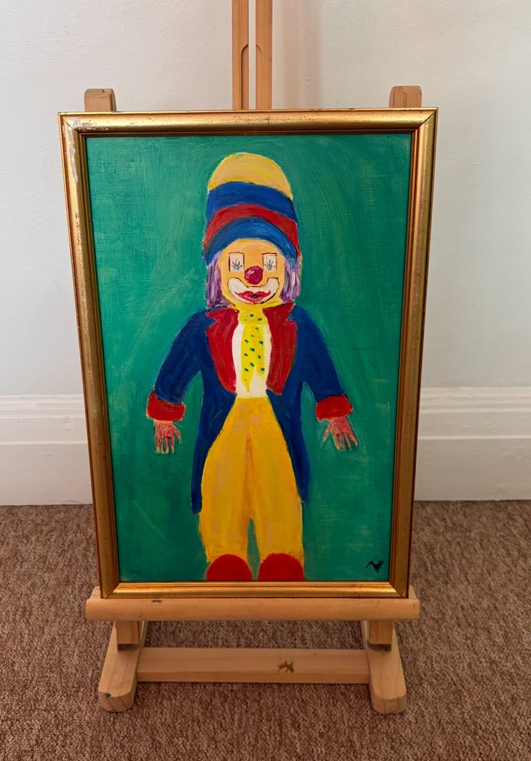Painting of a colorful clown with striped hat and red nose on green canvas displayed on wooden easel