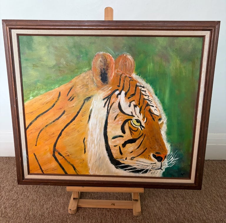Oil painting of a tigers head with orange and white fur displayed in a wooden frame on an easel