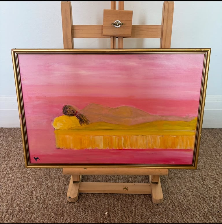 Framed painting on wooden easel depicting a brown figure resting on golden wheat field against pink sky