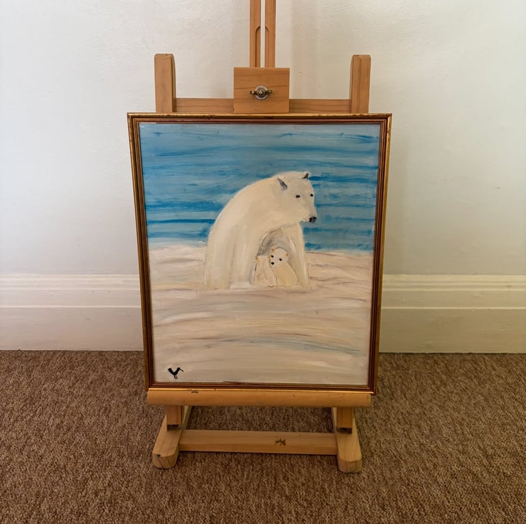 Painting on wooden easel depicting a mother polar bear with her cub on a beach by blue ocean water