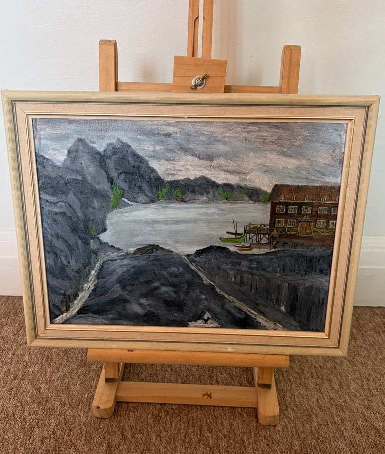 Framed landscape painting on wooden easel showing misty mountains, river, and riverside building with docks